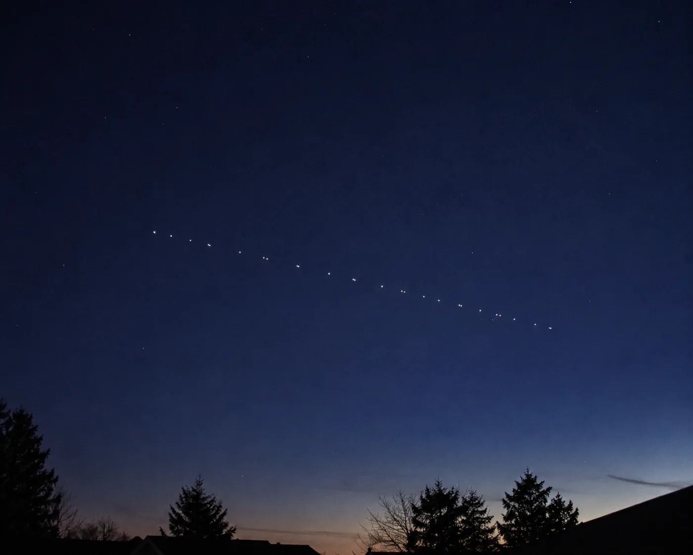 薄明の空を一列に横切るスターリンク衛星の列